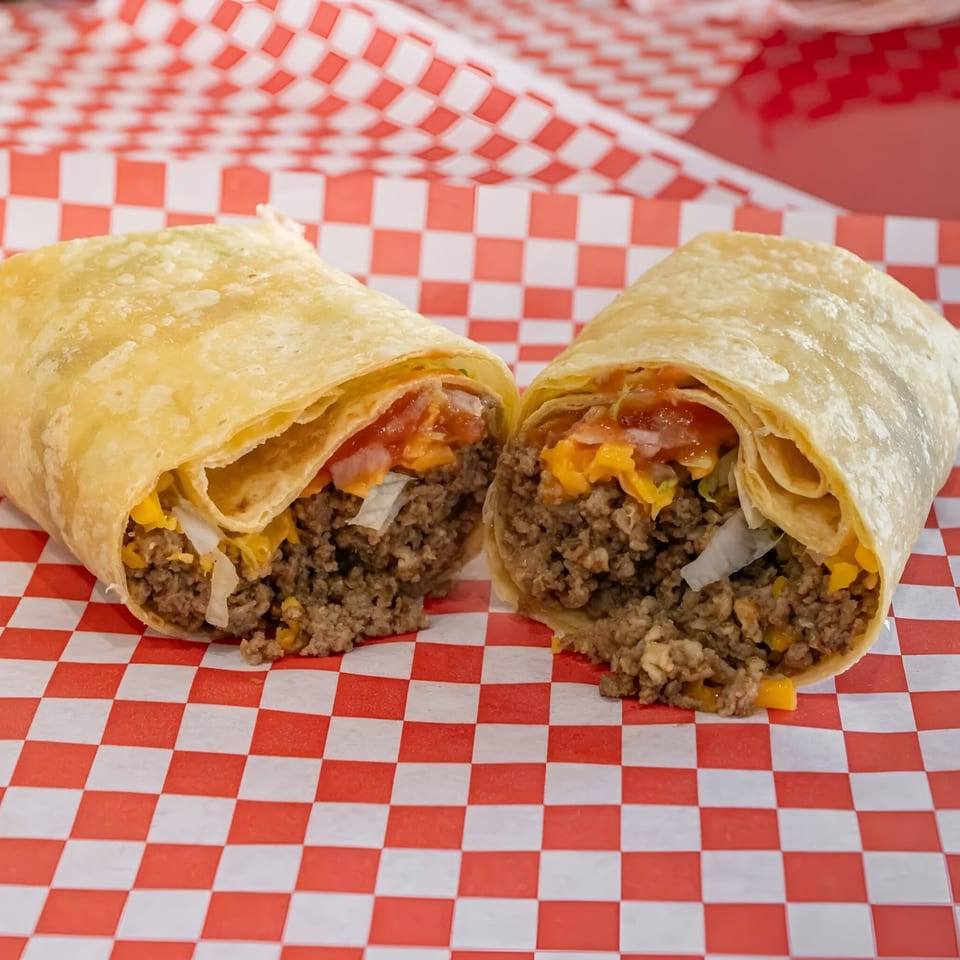 A beef burrito from Bobby's Place, cut in half, revealing ground beef, cheese, and salsa.