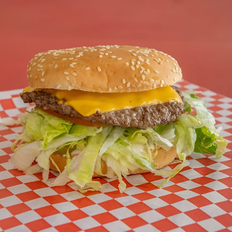 A Bobby's Place cheeseburger with lettuce and tomato on a red and white checkered paper.